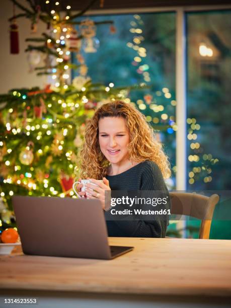 smiling woman having coffee while looking at laptop during christmas - christmas mug stock pictures, royalty-free photos & images
