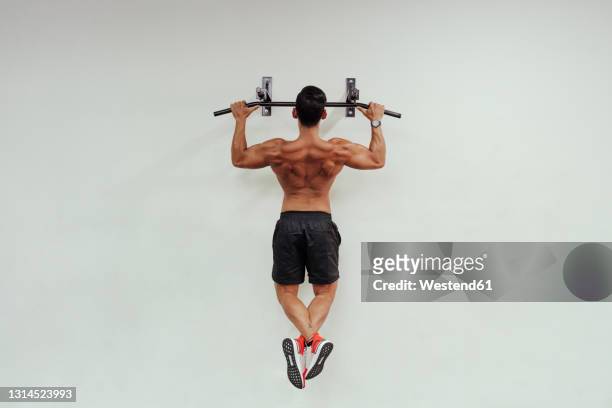 mid adult sportsman doing chin-ups with exercise equipment on white wall - pull ups stock pictures, royalty-free photos & images