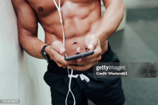 mid adult sportsman using mobile phone while leaning on wall at gym - tronco nu imagens e fotografias de stock