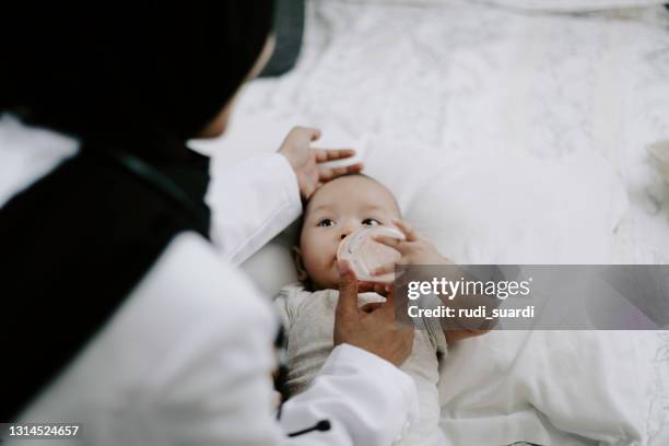 junger muslimischer arzt füttert ein baby - pediatric nurse stock-fotos und bilder