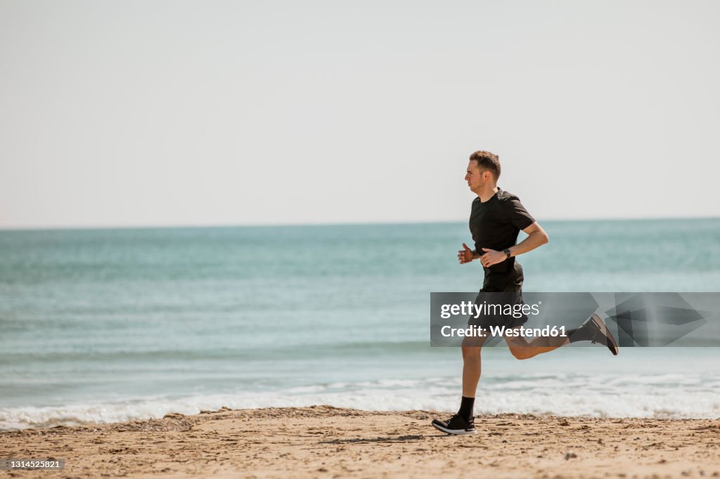Young man running at beach during sunny day