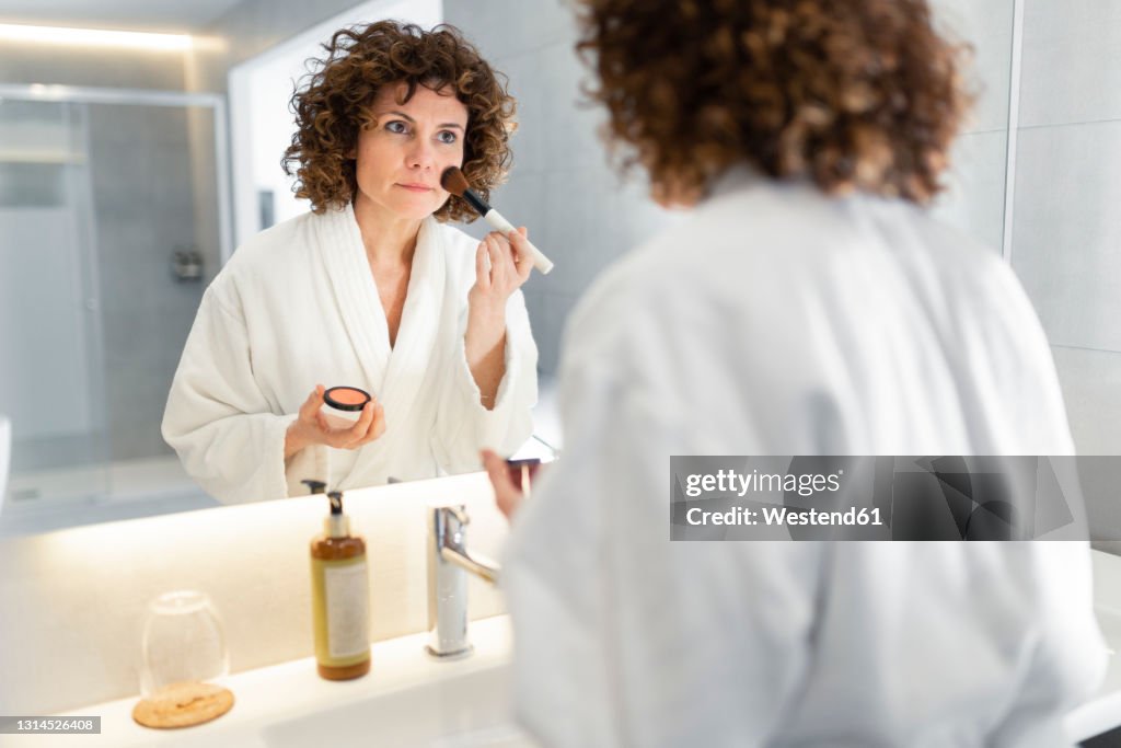 Beautiful woman applying powder from make-up brush in bathroom