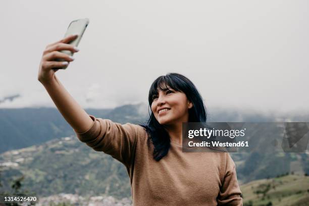 smiling mid adult woman taking selfie through mobile phone in front of sky - ecuador people stock pictures, royalty-free photos & images