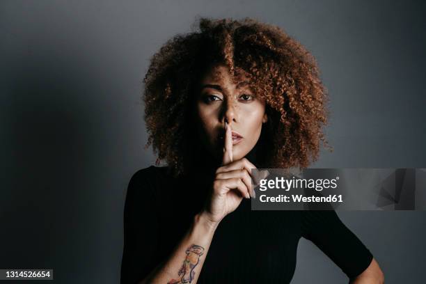 young woman with finger on lips over grey background - stilte stockfoto's en -beelden