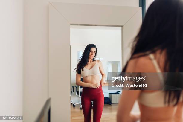 woman looking in mirror while adjusting pants in living room at home - bra fotografías e imágenes de stock