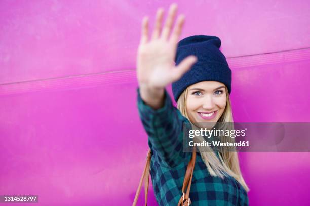 smiling woman showing stop gesture by pink wall - hand geste halt stock-fotos und bilder