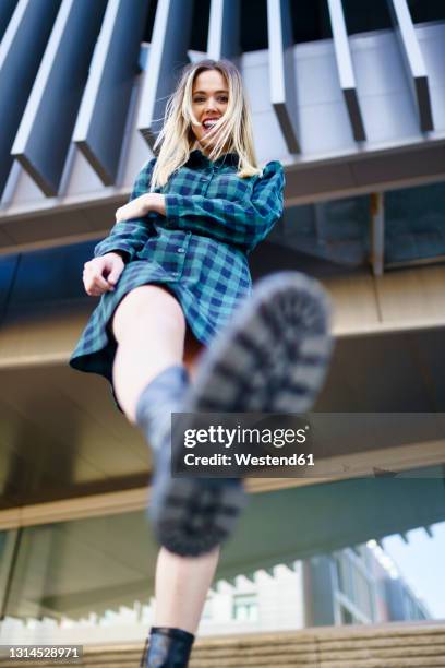 cheerful woman kicking in front of building - boot kicking stock pictures, royalty-free photos & images