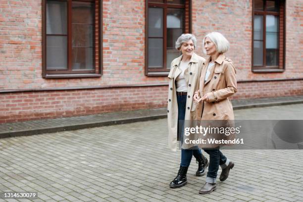 mature female friends walking on footpath - trench coat stock pictures, royalty-free photos & images