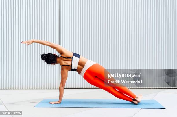 female sportswoman doing side plank pose in front of wall - woman front and back stockfoto's en -beelden