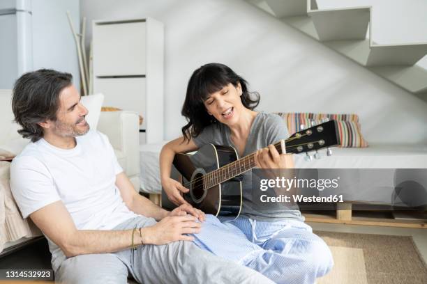 mature man looking at woman playing guitar at home - woman playing guitar stock pictures, royalty-free photos & images