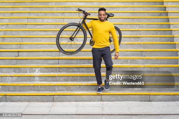 man carrying bicycle while moving down from staircase - man fallen up the stairs stock-fotos und bilder