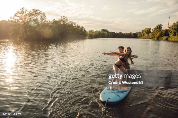 young couple enjoying summer at the lake, standing on a paddleboard - paddleboard stock pictures, royalty-free photos & images