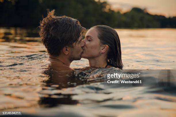 young couple swimming in lake, kissing at sunset - bisous photos et images de collection