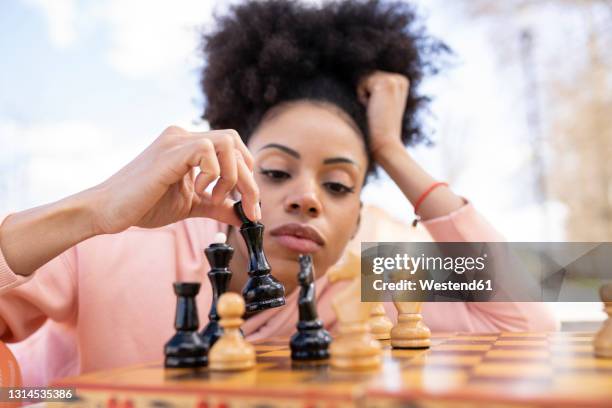 thoughtful woman with head in hand playing chess on table - chess stock pictures, royalty-free photos & images