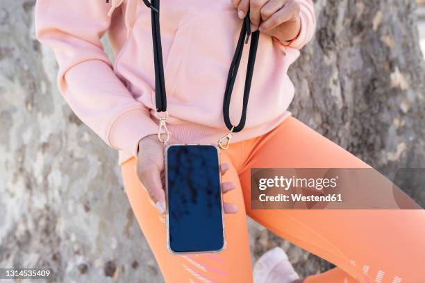 woman holding smart phone by tree - strap stock pictures, royalty-free photos & images