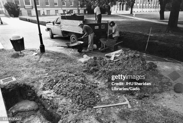 Outside the Milton S Eisenhower Library at Johns Hopkins University, construction workers use shovels and wheel barrows to dig a hole in the ground...