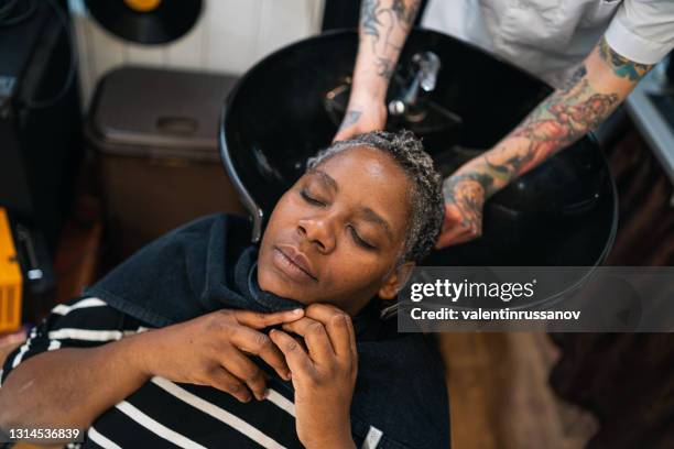 männlicher friseur waschen afro frau haare in einem friseursalon - afro man washing stock-fotos und bilder