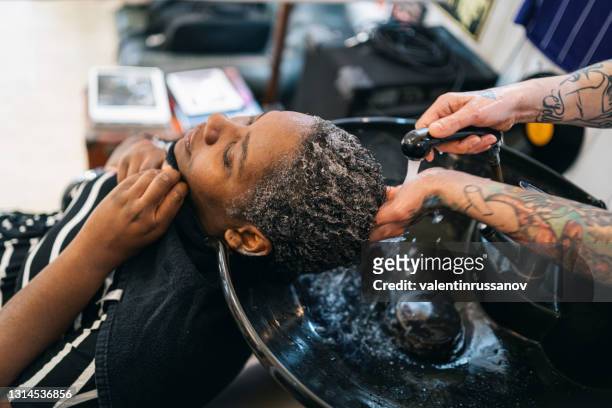 männlicher friseur waschen afro frau haare in einem friseursalon - afro man washing stock-fotos und bilder