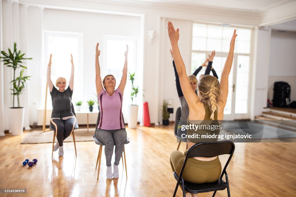 Female yoga instructor having yoga class with senior people on chairs