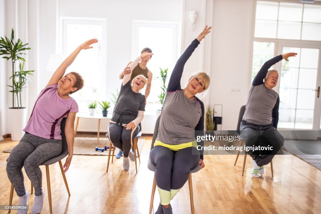 Aktive Senioren üben Yoga während Yoga-Kurs auf Stühlen