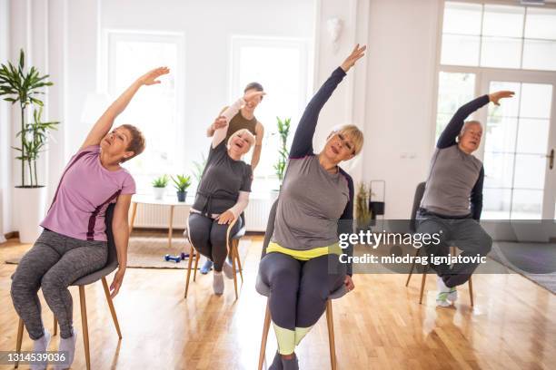 aktive senioren üben yoga während yoga-kurs auf stühlen - senior yoga stock-fotos und bilder