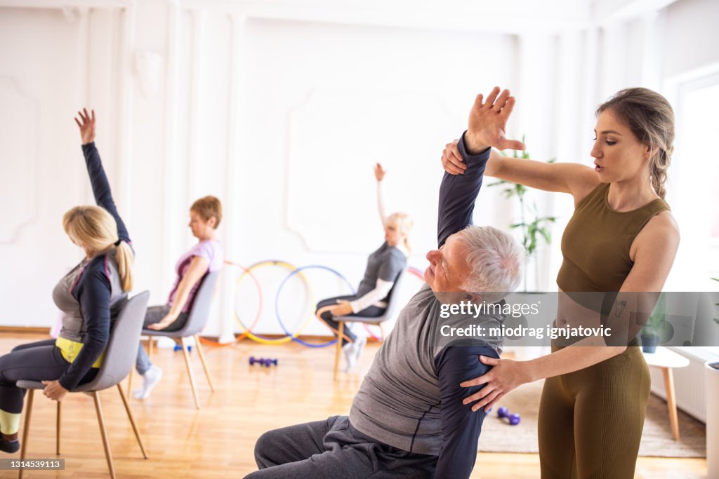 Yoga instructor assisting senior man during yoga class on chairs