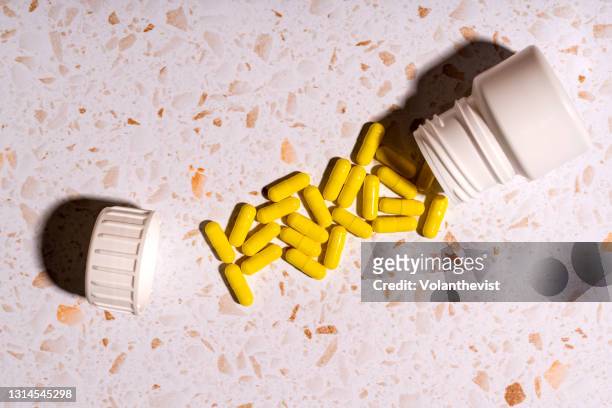 yellow pills out of the jar on a kitchen counter with mobile and plant - vitamins and minerals imagens e fotografias de stock