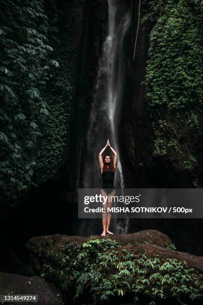 woman practicing yoga in forest in front of waterfall - klippenspringen stock-fotos und bilder