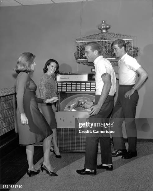 Two couples laughing and having a good time while dancing around jukebox. Circa 1955