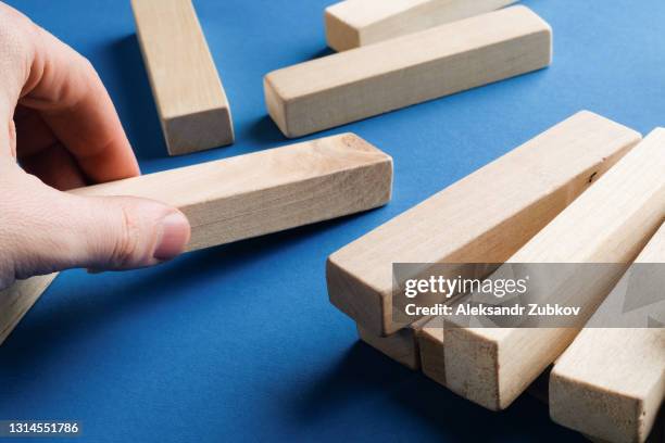 a pile of scattered wooden blocks on a blue background. a man picks up a piece or element of the game, tries to build a tower, to succeed. construction game. the ruined tower. - jenga stockfoto's en -beelden