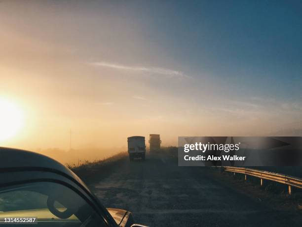 large trucks travelling along narrow road in fog at dawn. - kisumu stock pictures, royalty-free photos & images