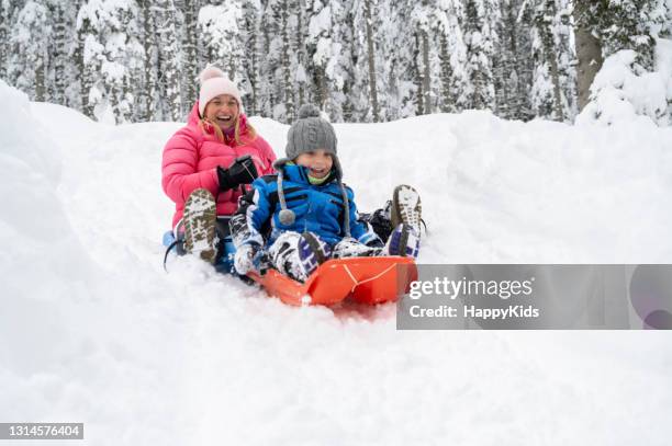 mother and son tobogganing on snowy landscape - family winter sport stock pictures, royalty-free photos & images