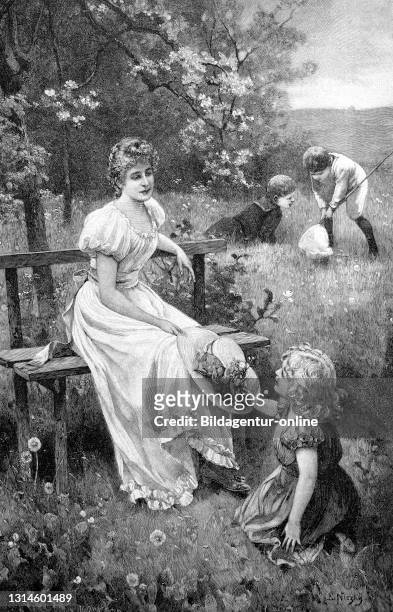 Mother with daughter in the spring in the open air, sitting on a bench, the girl playing on the lawn. In the background two boys to catch the...