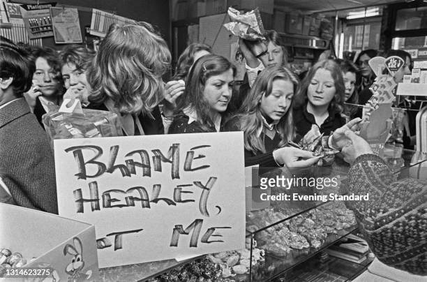 Children buying sweets in a shop which is displaying a sign reading 'Blame Healey, Not Me' after Budget Day, UK, 1st April 1974. Chancellor of the...