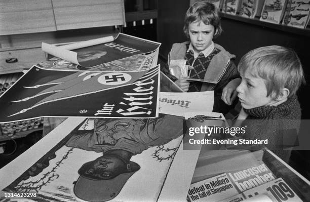 Two boys looking at German propaganda from World War II at the Imperial War Museum in London, UK, 26th March 1974. The top poster is an election...