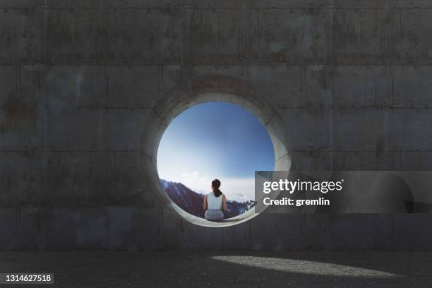 孤独な若い女性が座って、コンクリートの窓から見て - hole ストックフォトと画像