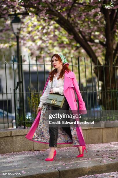 Nastasia Iavorscaia wears a green scarf over the head from Hermes, a bold pink long trench coat from Merry Perry, a white ruffle shirt / blouse with...