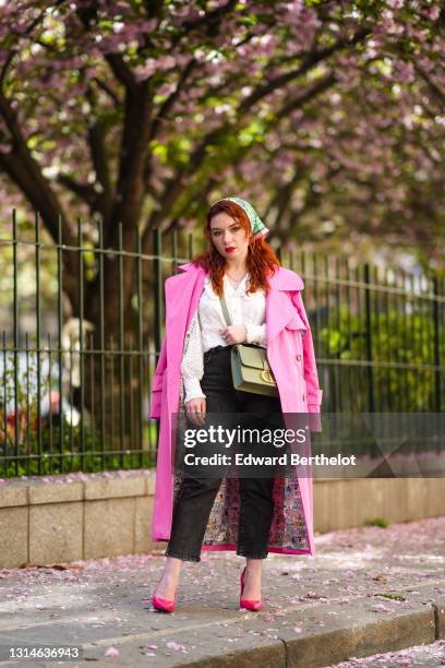 Nastasia Iavorscaia wears a green scarf over the head from Hermes, a bold pink long trench coat from Merry Perry, a white ruffle shirt / blouse with...