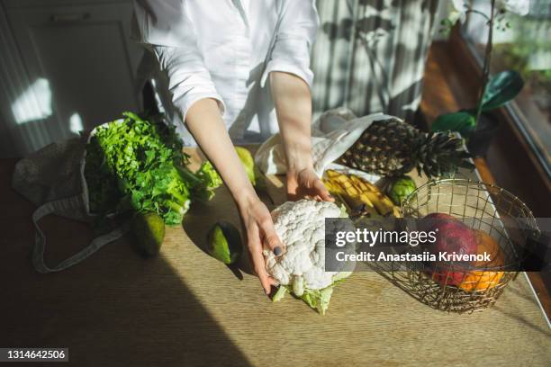 beautiful woman unpacks a full fabric bag with fruits and vegetables on the kitchen. - plant based diet stock pictures, royalty-free photos & images