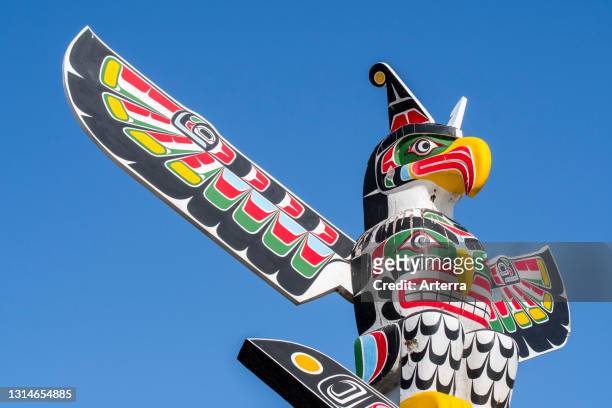 Colourful wooden carved Canadian totem pole showing eagle against blue sky.