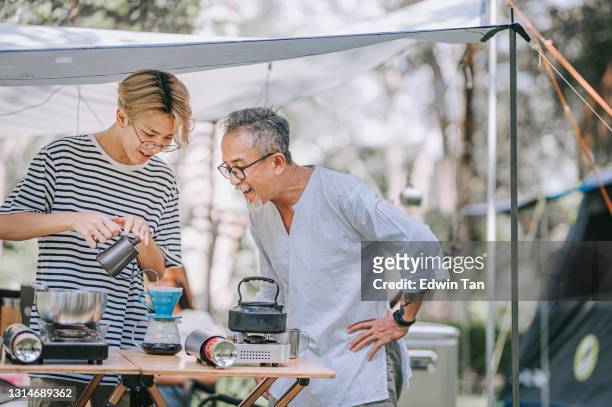 アジアの中国の10代の少年と父親は午後にキャンプテントで家族のためにコーヒーを滴下する準備をしています - やかん ��ストックフォトと画像