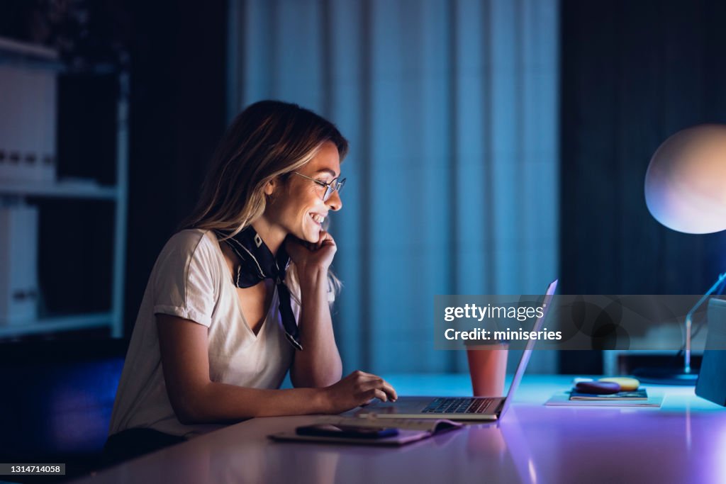 Cheerful lady with coffee and laptop in night