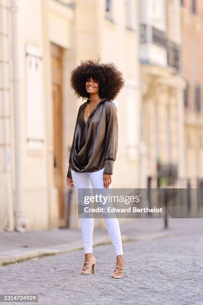 Alicia Aylies wears a khaki lustrous shiny silky low neck top with long sleeves, white skinny jeans, high heels shoes, on April 24, 2021 in Paris,...