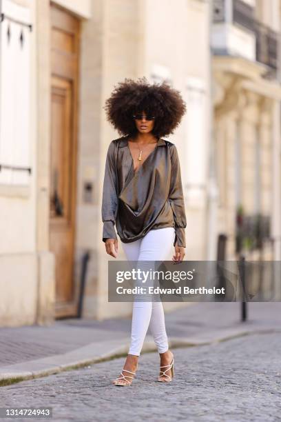 Alicia Aylies wears a khaki lustrous shiny silky low neck top with long sleeves, white skinny jeans, high heels shoes, on April 24, 2021 in Paris,...