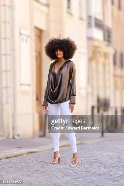 Alicia Aylies wears a khaki lustrous shiny silky low neck top with long sleeves, white skinny jeans, high heels shoes, on April 24, 2021 in Paris,...