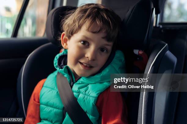 portrait of a 5 years old boy siting in safety car seat looking at camera with smiling face - schulkind nur jungen stock-fotos und bilder