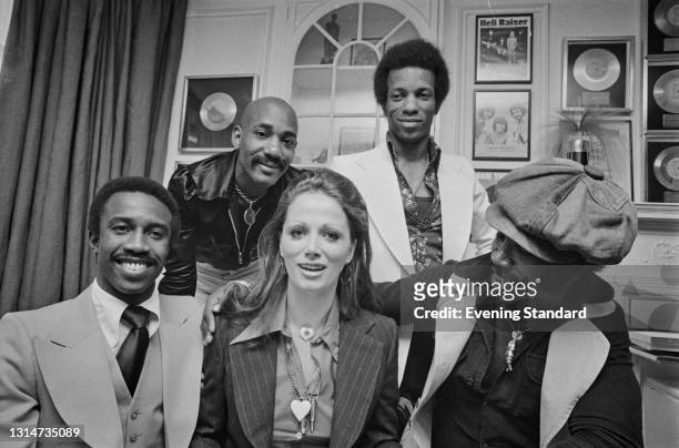 British soul band Hot Chocolate pose with English romance novelist Jackie Collins , UK, 7th June 1974. Collins is presenting the group with silver...