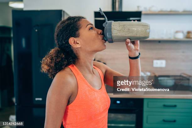 junge frau trinken protein shake nach dem training zu hause. - sport drinking bottle stock-fotos und bilder