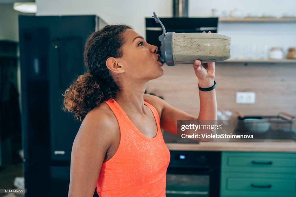 Jonge vrouw drinken eiwit shake na training thuis.