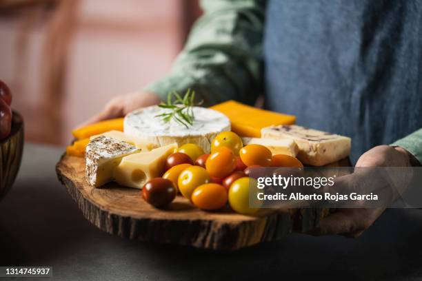 a man with a jeans apron with a cheese and tomatoes board - cheese plate stock-fotos und bilder